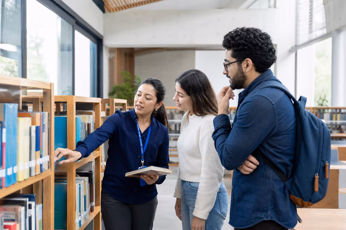 Bibliotecaria orientando a dos usuarios entre libros y estanterías de una biblioteca contemporánea